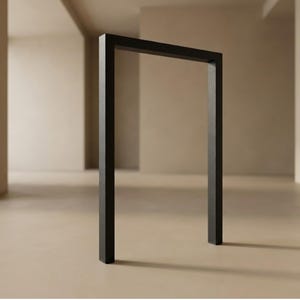 Puede incluir: Una estructura negra rectangular de marco abierto se encuentra en una habitación de tonos neutros. El marco está hecho de material oscuro y sólido, creando un fuerte contraste con el fondo claro. El diseño minimalista sugiere una estética moderna.
