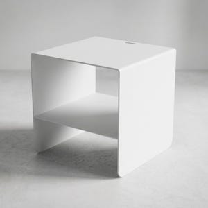 Minimalist metal side table CARINI in textured matte white steel, designed as a modern nightstand with open shelf for books, phone and bedside essentials, combining Italian craftsmanship, industrial design and premium bedroom furniture style.
