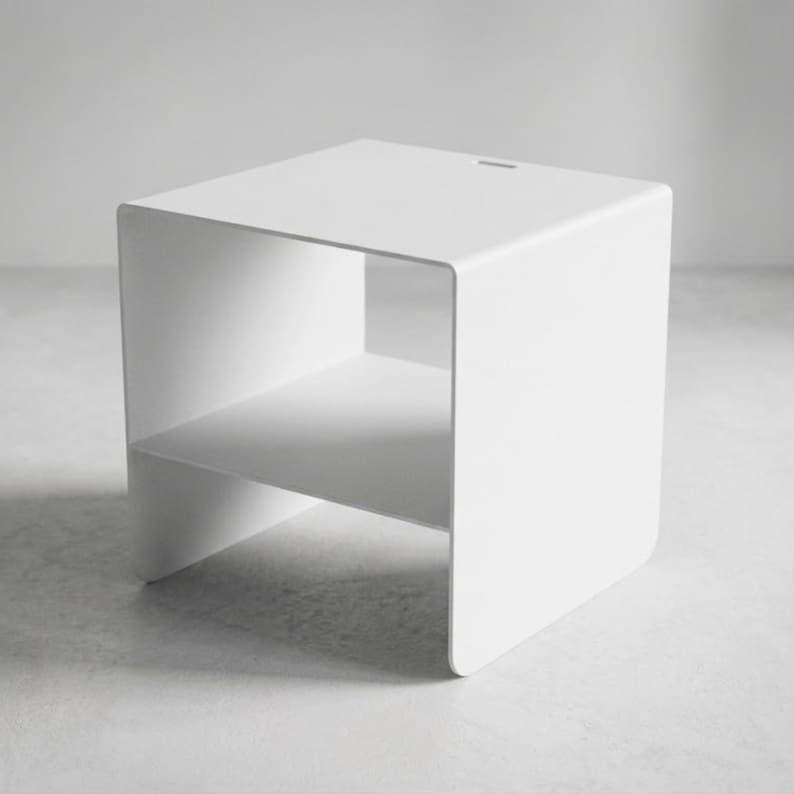 Minimalist metal side table CARINI in textured matte white steel, designed as a modern nightstand with open shelf for books, phone and bedside essentials, combining Italian craftsmanship, industrial design and premium bedroom furniture style.
