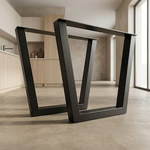 Può includere: Due gambe per tavolo in metallo nero con un design trapezoidale. Le gambe sono realizzate con tubi quadrati e sono progettate per sostenere un piano del tavolo. Le gambe sono mostrate su un pavimento in cemento di colore chiaro in un ambiente interno moderno.