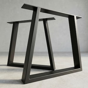 Op de afbeelding: Twee zwarte metalen tafelpoten met een modern, geometrisch ontwerp. De poten hebben een rechthoekige basis en een trapeziumvorm, met een platte bovenkant voor het bevestigen van een tafelblad. De poten zijn gemaakt van stevig metaal en geschikt voor diverse tafelmaten.