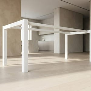 Può includere: Un tavolo rettangolare bianco moderno dal design minimalista. Il tavolo ha quattro gambe quadrate e un telaio con due supporti orizzontali. Il tavolo è ambientato in uno spazio aperto e luminoso con pavimento in legno chiaro.