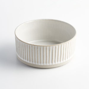 May include: White ceramic bowl with a ribbed design. The bowl is round and has a smooth, white interior.