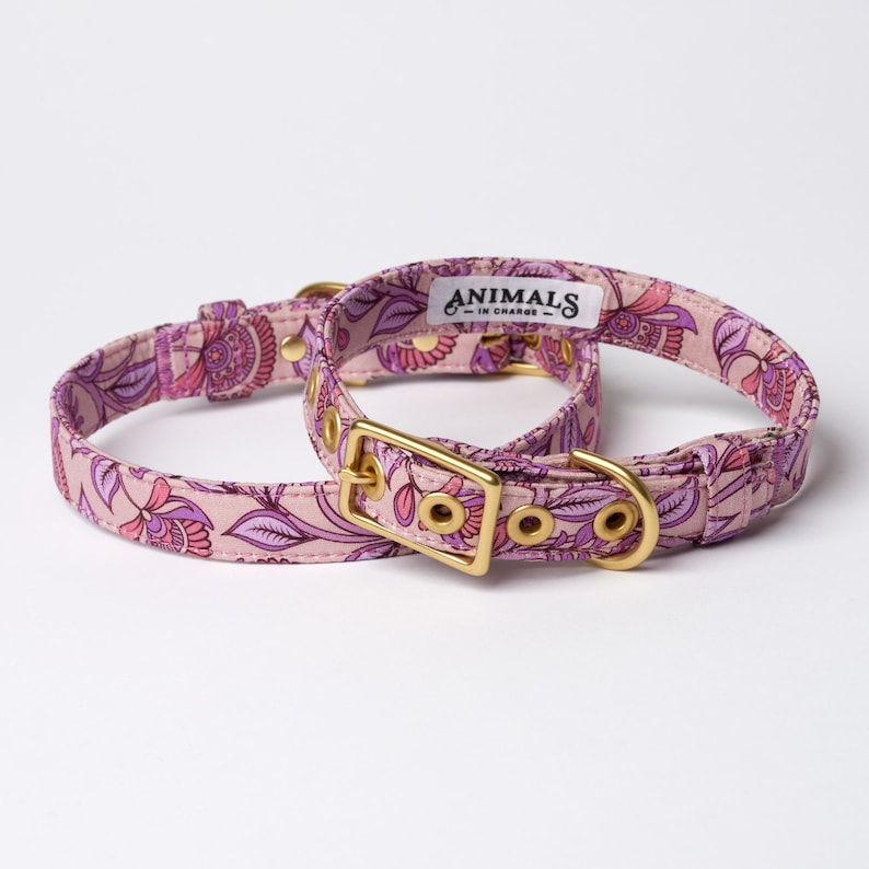 Pu&ograve; includere: Due collari per cani rosa con motivo floreale. I collari hanno una ferramenta in metallo dorato, tra cui una fibbia e un anello a D. Il collare pi&ugrave; grande ha un'etichetta bianca con la scritta "ANIMALS - IN CHARGE - ".