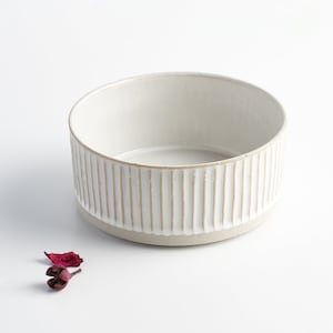 May include: A white ceramic bowl with a ribbed design. The bowl is round and has a smooth, white interior.