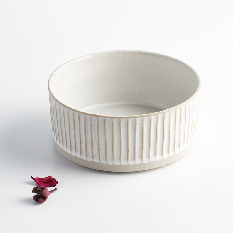 May include: A white ceramic bowl with a ribbed design. The bowl is round and has a smooth, white interior.