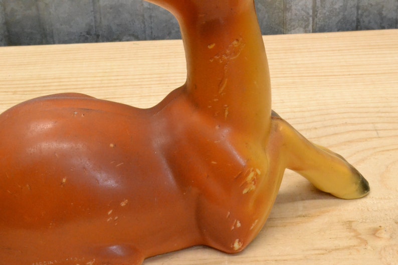 May include: A ceramic deer figurine in a lying down position. The deer is brown and yellow with a textured surface.