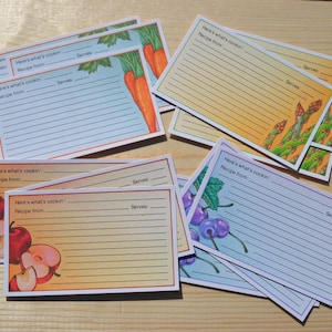 May include: Recipe cards with colorful illustrations of fruits and vegetables, including carrots, apples, cherries, and asparagus. Each card has lines for writing a recipe, with the text "Here's what's cookin'" and "Recipe from:" printed on them.