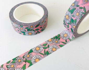 Può includere: Nastro washi rosa con un motivo di margherite bianche e foglie verdi. Il nastro è arrotolato su un rotolo.