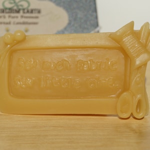 May include: A light brown rectangular bar of soap with the words "Sew much fabric, sew little time" embossed on the front. The soap is decorated with a small spool of thread and a pair of scissors.