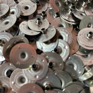 May include: A pile of silver metal candle holders with a small hole in the center of each. The holders are round and have a slightly raised edge.