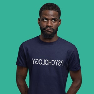 May include: Navy blue t-shirt with the word "PSYCHOLOGY" printed in white, upside down. The shirt is worn by a person with a beard, against a teal background.