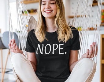 May include: A woman wearing a black t-shirt with the word "NOPE" printed in white on the front. She is sitting in a white hammock with her eyes closed and a relaxed expression.
