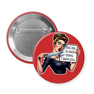 May include: A red button badge featuring a vintage-style illustration of a woman holding a knife and a sign with the text "Tell me to calm down. I dare you." The badge has a silver metal back.