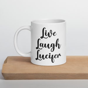May include: White ceramic coffee mug with black text that reads "Live Laugh Lucifer".