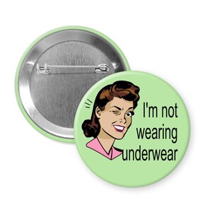 May include: A light green button with a retro illustration of a winking woman. The text "I'm not wearing underwear" is printed in black. The button has a silver pin back.