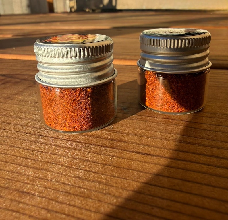 Pu&ograve; includere: Due piccoli barattoli di vetro trasparente riempiti con una spezia finemente macinata di un vibrante colore rosso-arancio. Ogni barattolo &egrave; dotato di un tappo a vite in metallo argentato e zigrinato. I barattoli sono posizionati fianco a fianco.