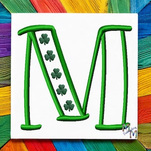 May include: Green embroidered letter M with shamrocks on the diagonal line of the letter. The letter is on a white background.