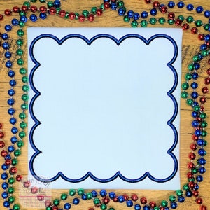 May include: A white square with a scalloped border in shades of blue and purple. The border is outlined in black. The square is on a wooden surface.