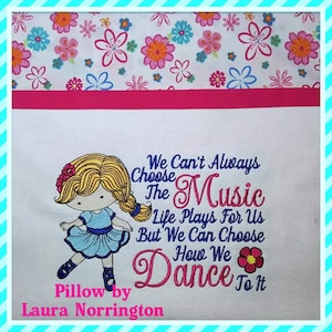 May include: Embroidered pillow with a cartoon girl in a blue dress dancing. The text reads "We Can't Always Choose The Music Life Plays For Us But We Can Choose How We Dance To It". The pillow is decorated with a pink flower and the text "Pillow by Laura Norrington".