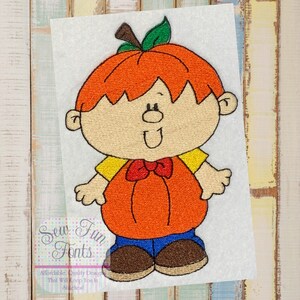 Pode incluir: Desenho bordado de uma criança sorridente vestida de abóbora. A criança está usando uma camisa amarela, uma gravata borboleta vermelha, calças azuis e sapatos marrons. A abóbora é laranja com um caule e uma folha verdes.