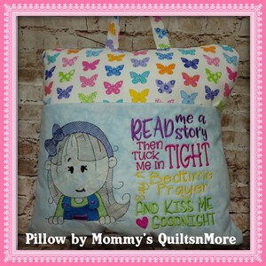 Puede incluir: Una almohada azul y blanca con un bolsillo en la parte delantera. El bolsillo tiene bordado un rostro de niña, junto con el texto "READ me a story Then TUCK me in TIGHT Say Bedtime Prayer AND KISS ME GOODNIGHT". La almohada está decorada con un patrón de mariposas.