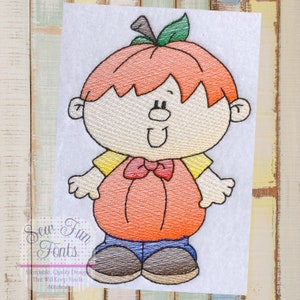 Pode incluir: Desenho bordado de uma criança vestida de abóbora para o Halloween. A criança está vestindo uma camisa amarela, um traje de abóbora laranja, calças azuis e sapatos marrons. A criança tem cabelo ruivo e um grande sorriso.