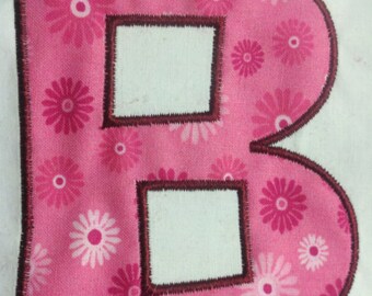 May include: A pink fabric letter B with a brown outline. The fabric has a white and pink floral pattern.