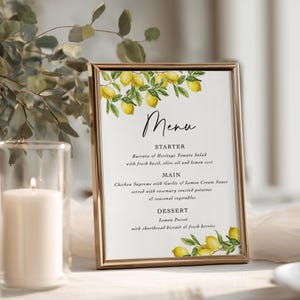 May include: A vertical rectangular menu card in a thin gold frame, featuring a watercolor illustration of yellow lemons and green leaves at the top and bottom. The text reads Menu, Starter, Burrata & Heritage Tomato Salad, Main, Chicken Supreme, and Dessert.