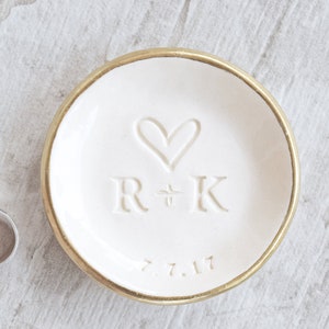 gold rim 3.5 inch glossy white ceramic wedding ring dish engraved with large heart, 2 name initials & date. Minimalist white on white design hand stamped clay pottery personalized wedding gift, wife anniversary present, jewelry trinket holder bowl