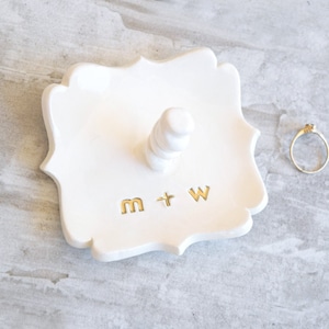 Four inch wide fancy square dish Handcrafted pottery ceramic jewelry storage tray with 2 inch tall ring post in center. Engraved with 2 custom gold monogram initials letters for personalized wedding ring holder engagement gifts for couples.