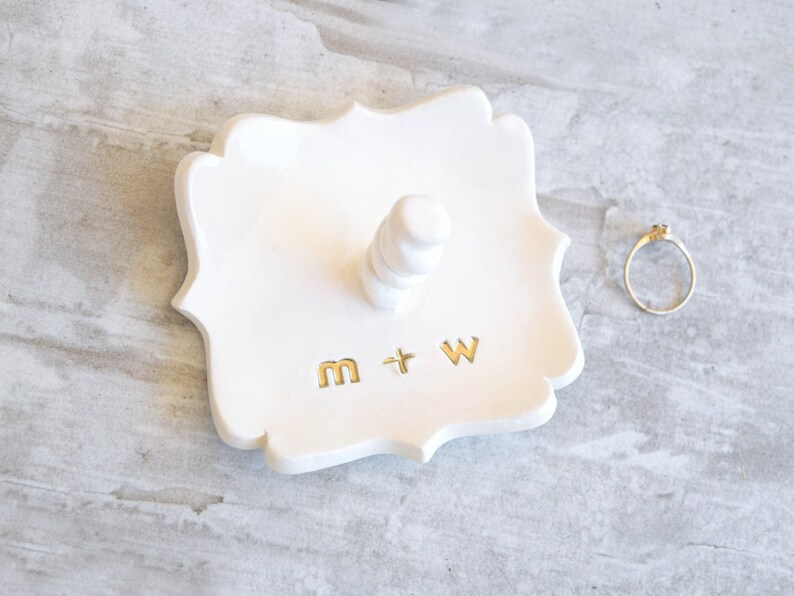 Four inch wide fancy square dish Handcrafted pottery ceramic jewelry storage tray with 2 inch tall ring post in center. Engraved with 2 custom gold monogram initials letters for personalized wedding ring holder engagement gifts for couples.