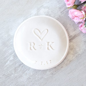 modern 3.5 inch glossy white ceramic wedding ring dish engraved with large heart, 2 name initials & date. Minimalist white on white design hand stamped clay pottery personalized wedding gift, wife anniversary present, jewelry trinket holder bowl