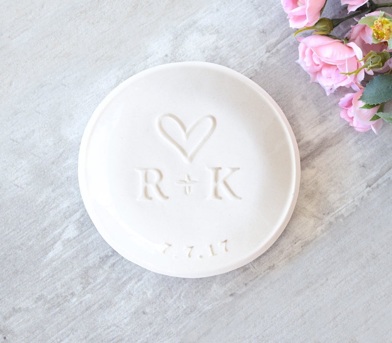 modern 3.5 inch glossy white ceramic wedding ring dish engraved with large heart, 2 name initials & date. Minimalist white on white design hand stamped clay pottery personalized wedding gift, wife anniversary present, jewelry trinket holder bowl