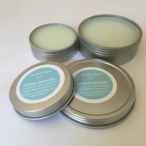 May include: Four silver-colored tins of Boo Boo Balm, filled with a pale green balm. Two tins have labels that read "Boo Boo Balm" and "leabee naturals". The labels also include the text "Works on everything but a broken heart :)".