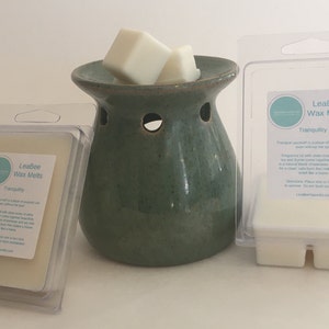 Op de afbeelding: Een set wax melts in een doorzichtige plastic verpakking met het label "LeaBee Wax Melts Tranquility". De wax melts zijn wit en bevinden zich in een keramische wax warmer met een groene glazuur.