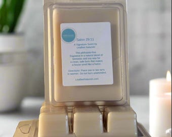 Op de afbeelding: Een doorzichtige plastic container met drie wasblokjes erin. De wasblokjes zijn lichtbruin van kleur. De container heeft een label met de tekst "Salon 29:11 A Signature Scent by LeaBee Naturals".