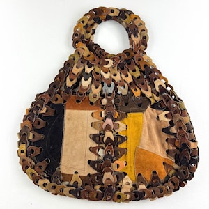May include: A brown leather handbag with a unique design. The bag is made of small, interconnected leather pieces that form a chain-like pattern. The bag has a top handle and is made of various shades of brown leather.