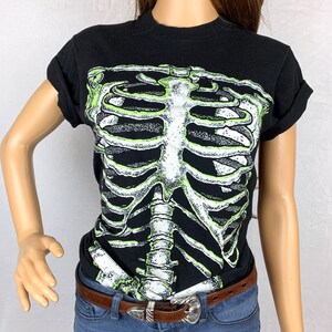 Op de afbeelding: Zwart T-shirt met een groene en witte skeletprint.