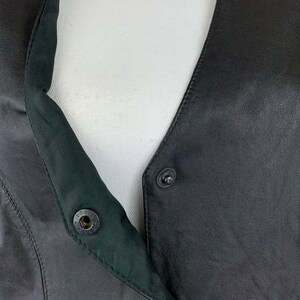 May include: Black leather vest with a snap closure and a green lining. The vest has a V-neck and a button closure at the top.