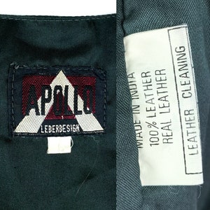 May include: A dark green leather jacket with a white label that reads "MADE IN INDIA 100% LEATHER REAL LEATHER LEATHER CLEANING". The jacket also has a black and white label that reads "APOLLO LEDERDESIGN".