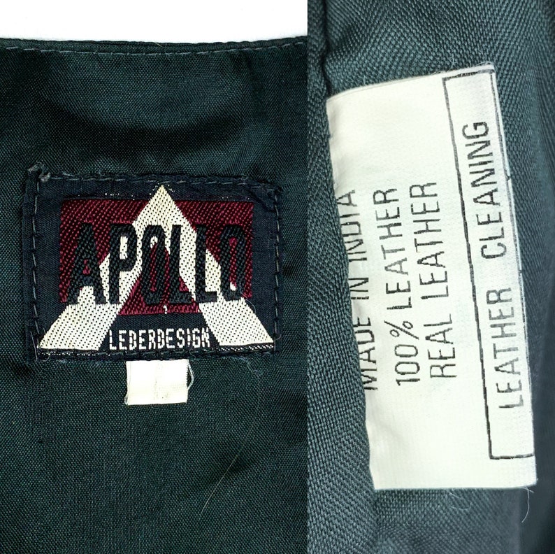 May include: A dark green leather jacket with a white label that reads "MADE IN INDIA 100% LEATHER REAL LEATHER LEATHER CLEANING". The jacket also has a black and white label that reads "APOLLO LEDERDESIGN".