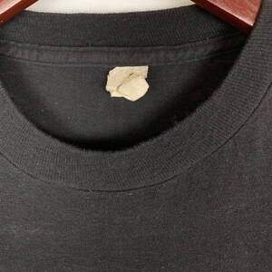Op de afbeelding: Zwart T-shirt met een groene en witte grafische print. Het shirt heeft een label op de hals.