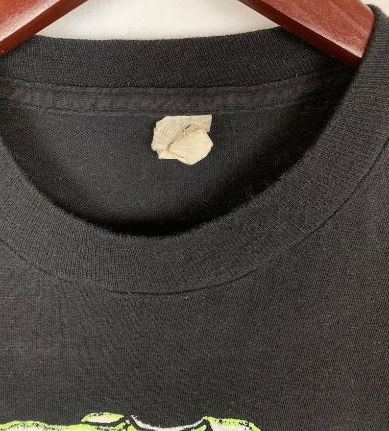 Op de afbeelding: Zwart T-shirt met een groene en witte grafische print. Het shirt heeft een label op de hals.