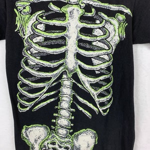 Op de afbeelding: Zwart T-shirt met een groene en witte skeletprint op de voorkant.