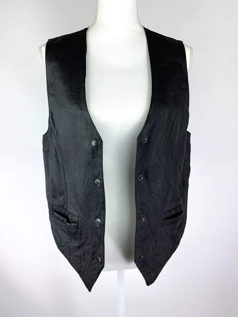 May include: A black leather vest with a V-neck and multiple button fastenings. The vest has two pockets on the front.