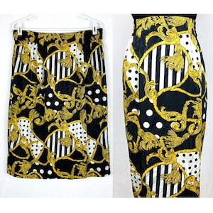 May include: Black skirt with a gold, white, and black patterned design. The pattern features a repeating design of gold chains, white polka dots, and black and white stripes.