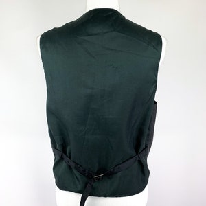 May include: A dark green sleeveless waistcoat with a black adjustable strap at the back.