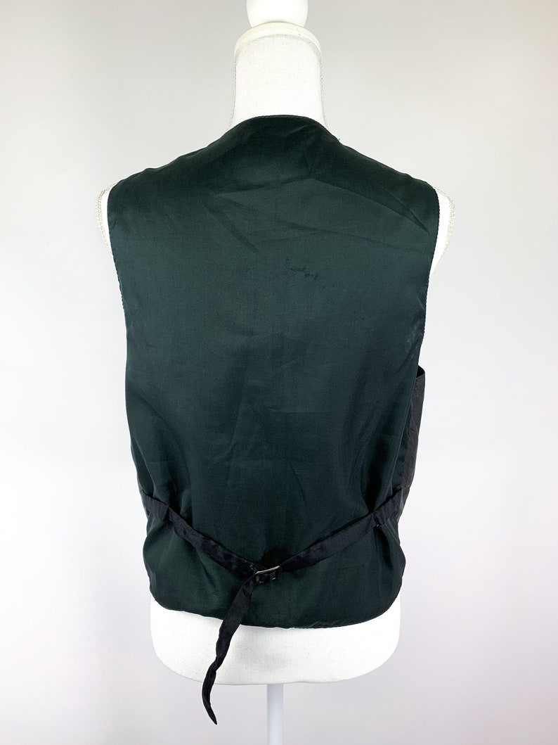 May include: A dark green sleeveless waistcoat with a black adjustable strap at the back.
