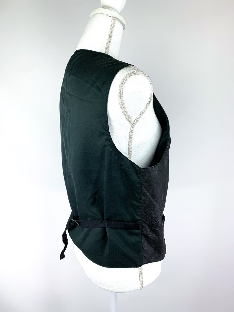 May include: A dark green waistcoat with a black satin back panel and a black adjustable strap. The waistcoat has a classic design and is made of a smooth fabric.